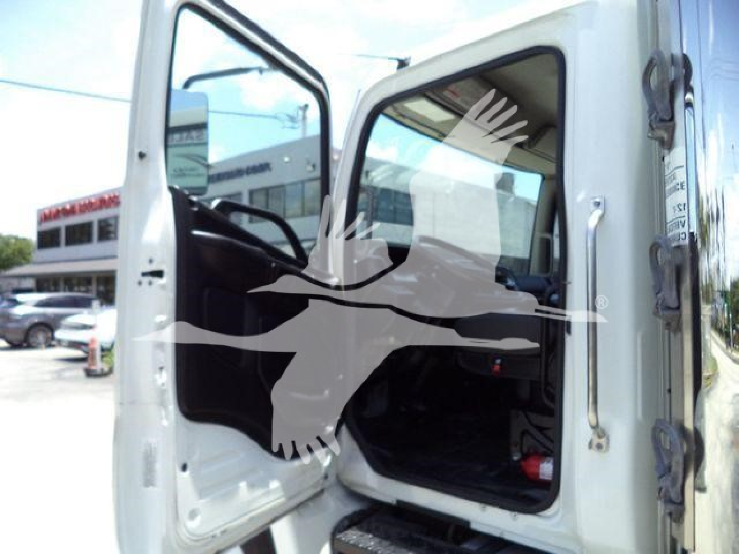 Truck cab interior with open door, 2019 Hino 268A refrigerated truck, frontview showing driver seat and steering wheel.