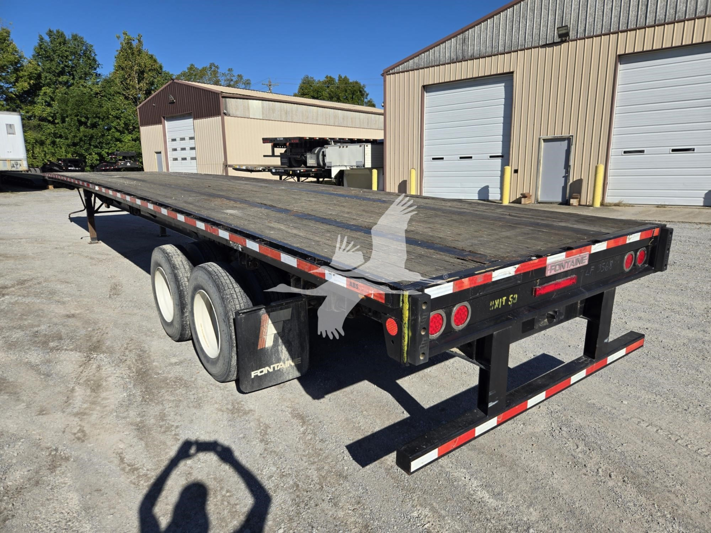 Flatbed trailer showing dual rear axles and wooden deck with reflectors, Fontaine branding on mud flaps, red/white safety striping along edges.