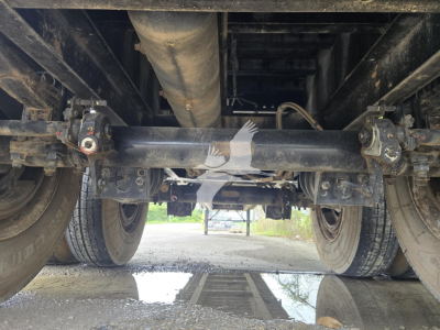Underneath view of a 2017 Fontaine steel flatbed trailer showing the rear axle, suspension, and leaf springs with a central driveshaft and connected components.