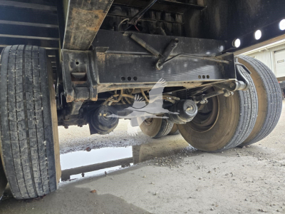Flatbed trailer underside showing axle and suspension components with tires visible and a puddle underneath.
