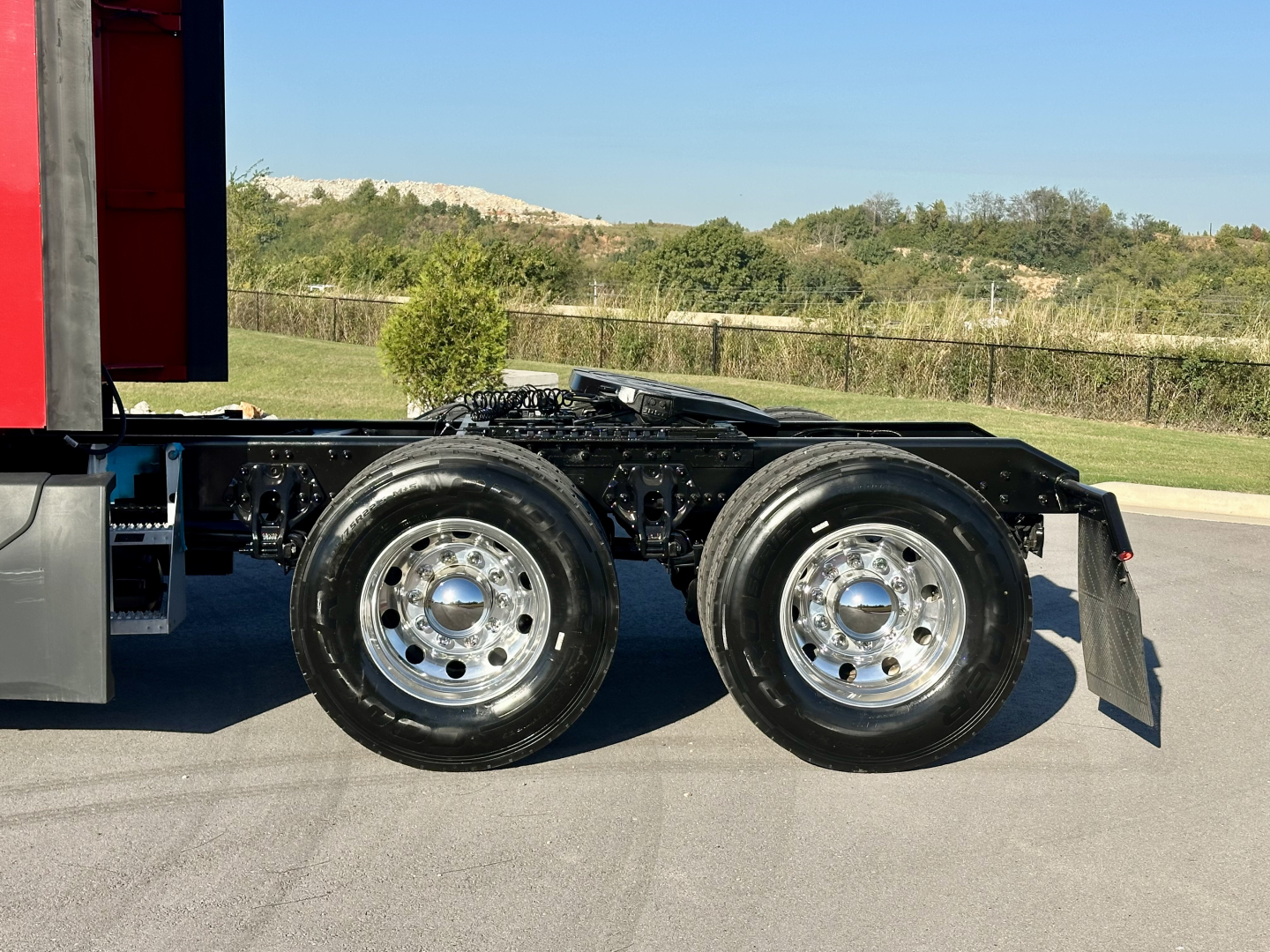 Kenworth truck chassis with dual rear axles and aluminum wheels, side view showing truck frame and wheels.
