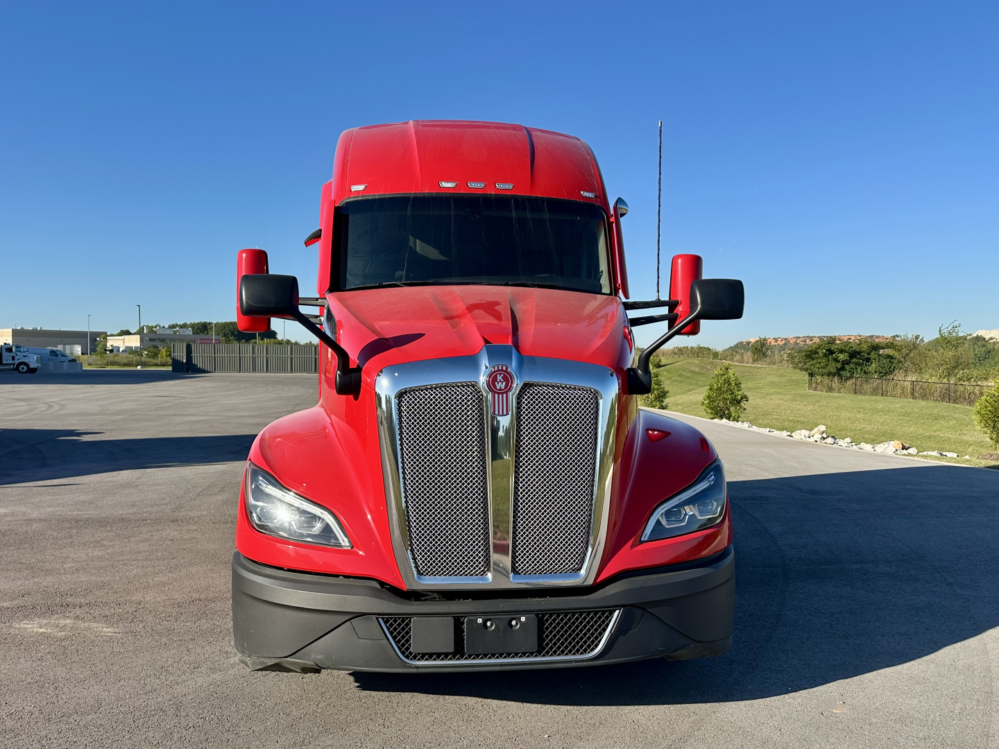 Kenworth T680 truck front view showing bright red cab with large chrome grille and black bumper.