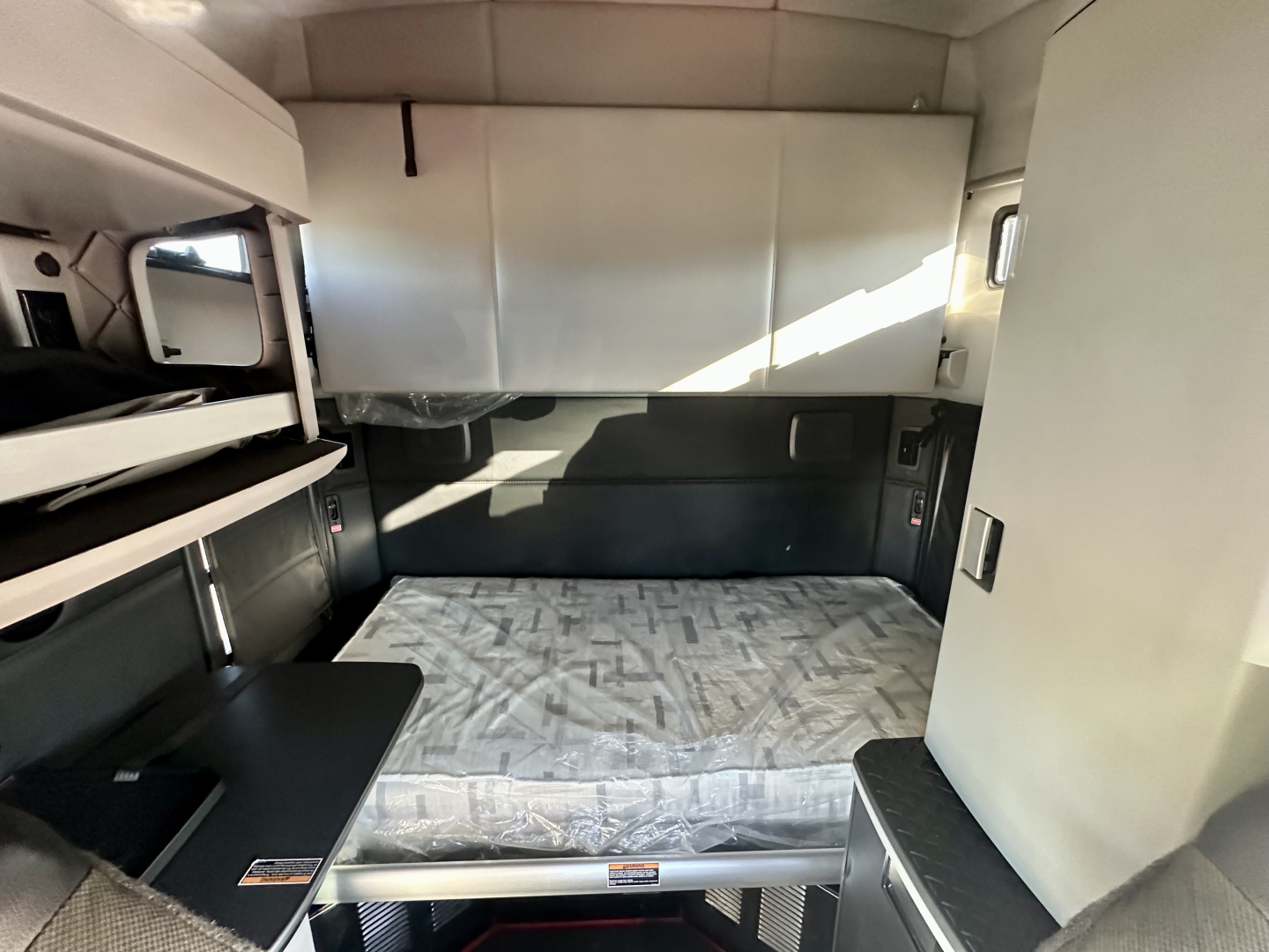 Kenworth T680 sleeper cab interior showing bunk area and storage with light coming through window.