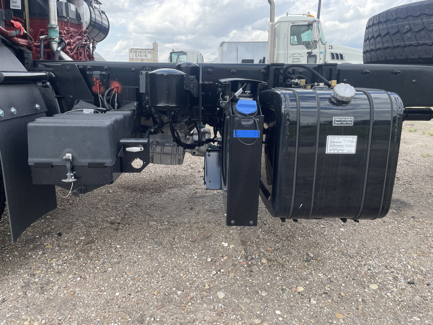 Truck chassis showing fuel tank and hydraulic reservoir with blue label and wiring harnesses.