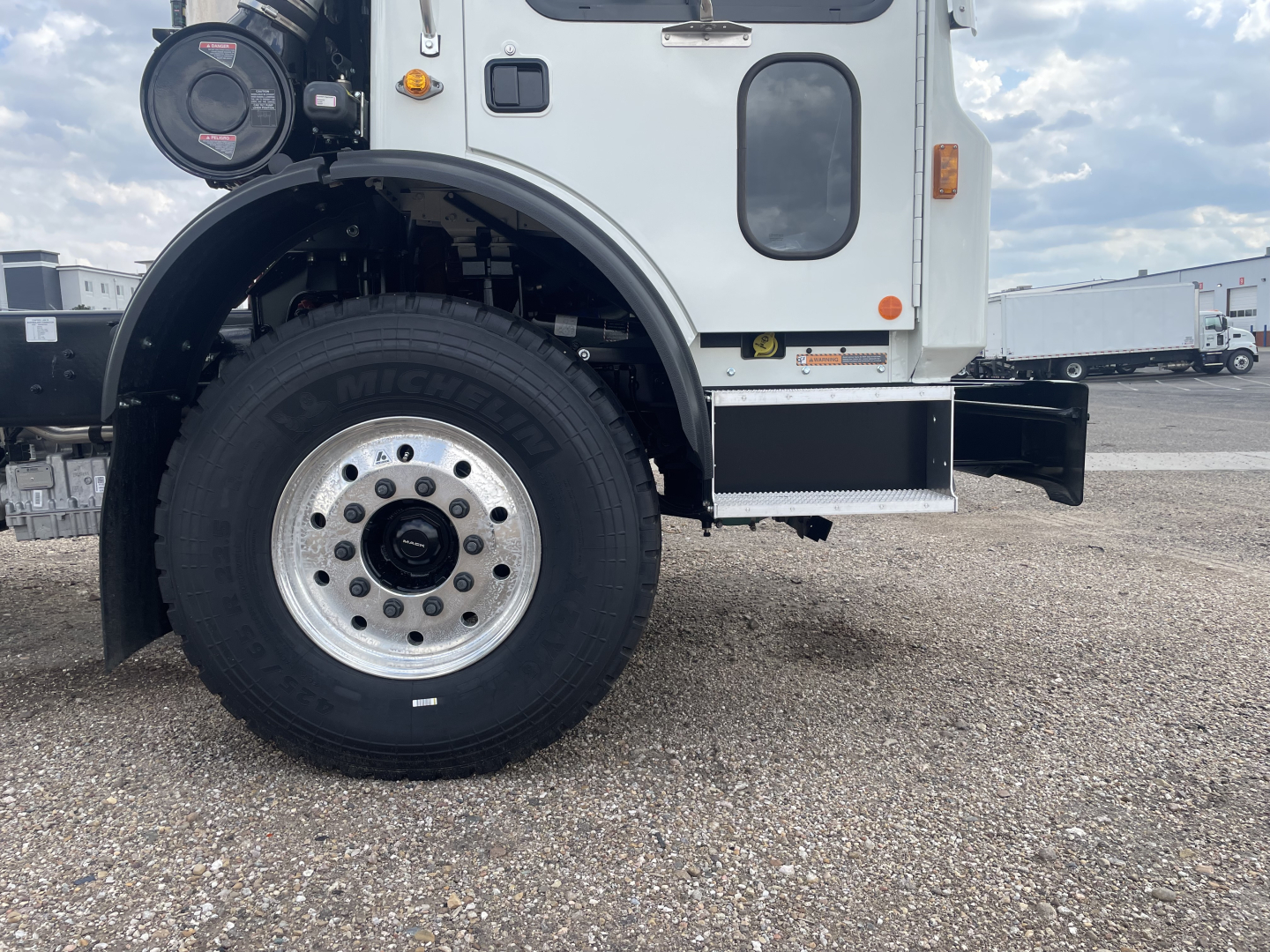 Front left wheel and cab side of a Mack TE64 truck showing Michelin tire, wheel, fender, and steps.
