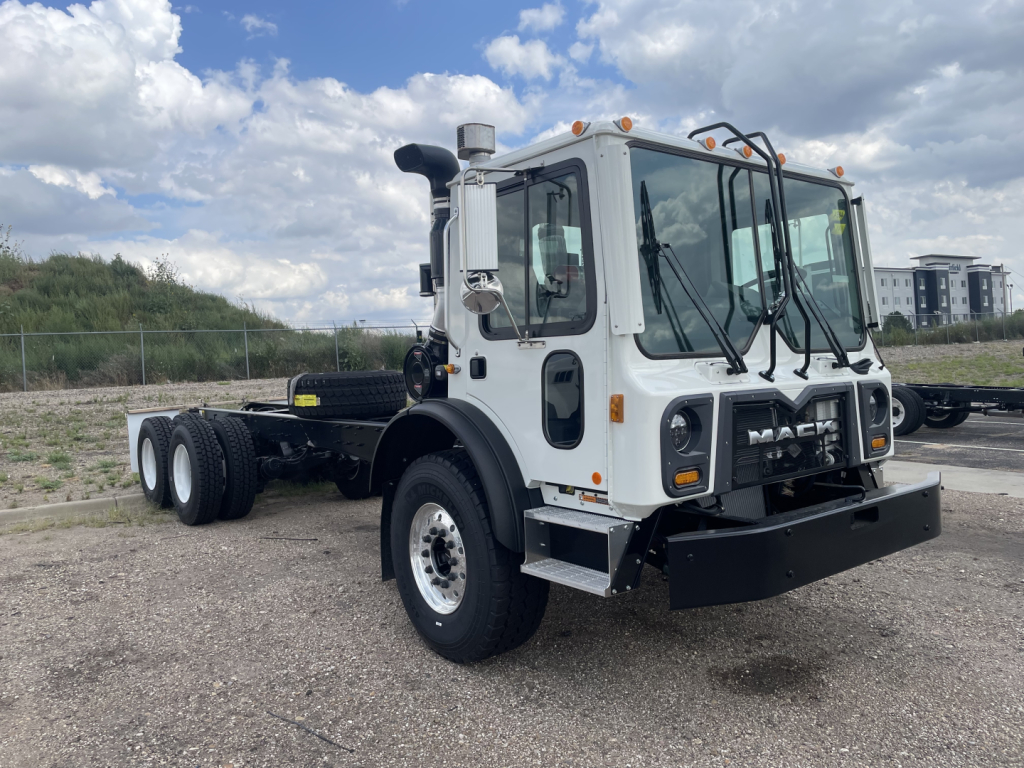 Mack TE64 cab and chassis showing front view with black bumper and white cab, six-wheel configuration, Mack logo on grille, windshield wipers, and side mirrors.