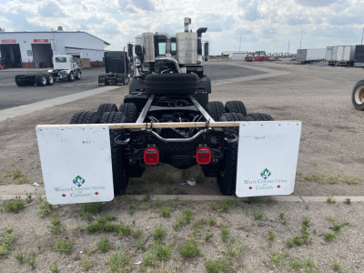 Rear view of a new 2026 Mack TE64 truck chassis showing dual white mud flaps with Waste Connections Canada logos, rear lights, and spare tire mounted between the chassis.
