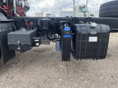 Truck chassis showing fuel tank and hydraulic reservoir with blue label and wiring harnesses.