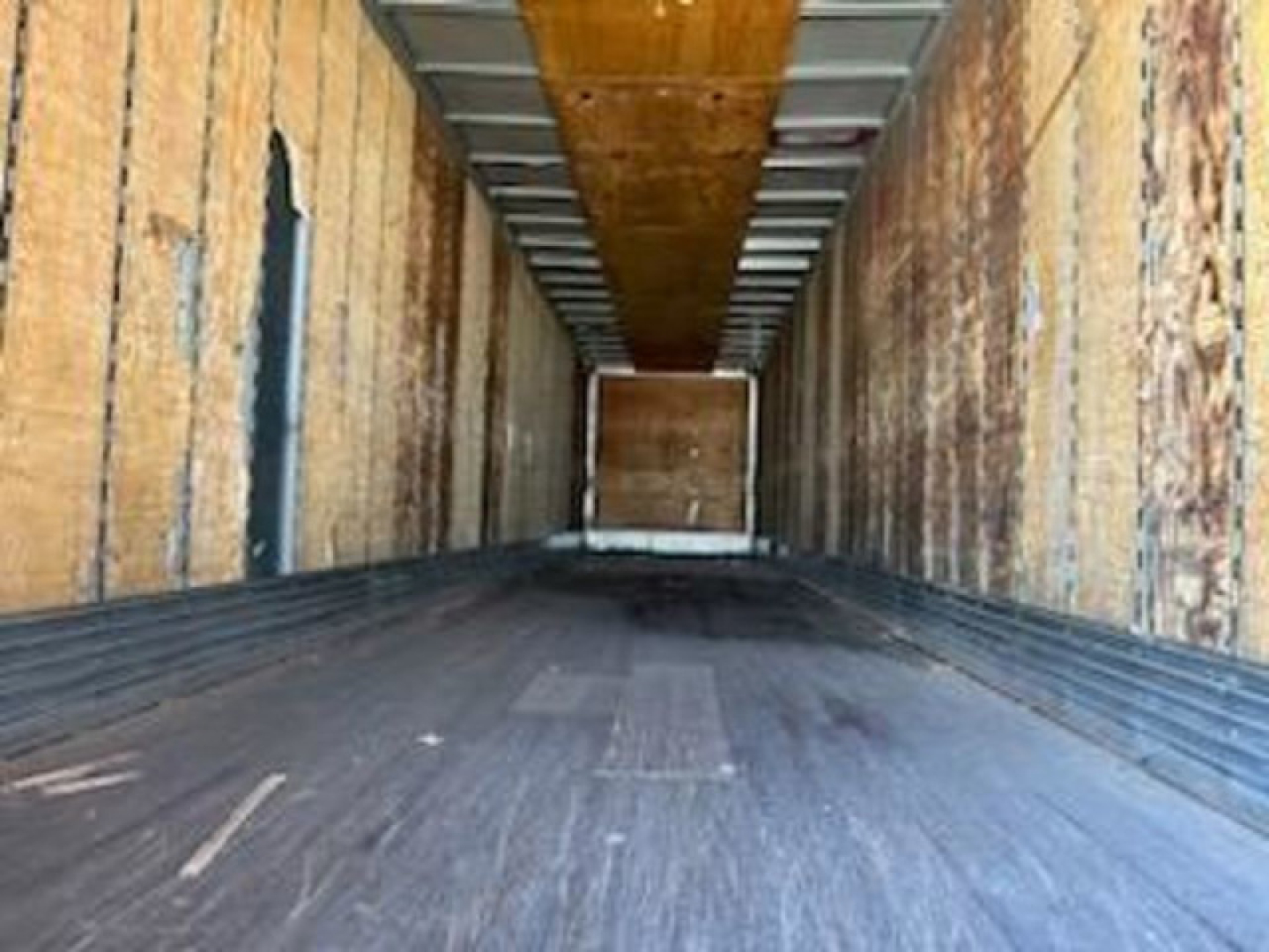 Interior of a Trailmobile van trailer showing wooden sidewalls and dark floor, empty cargo area, rear ramp door visible.