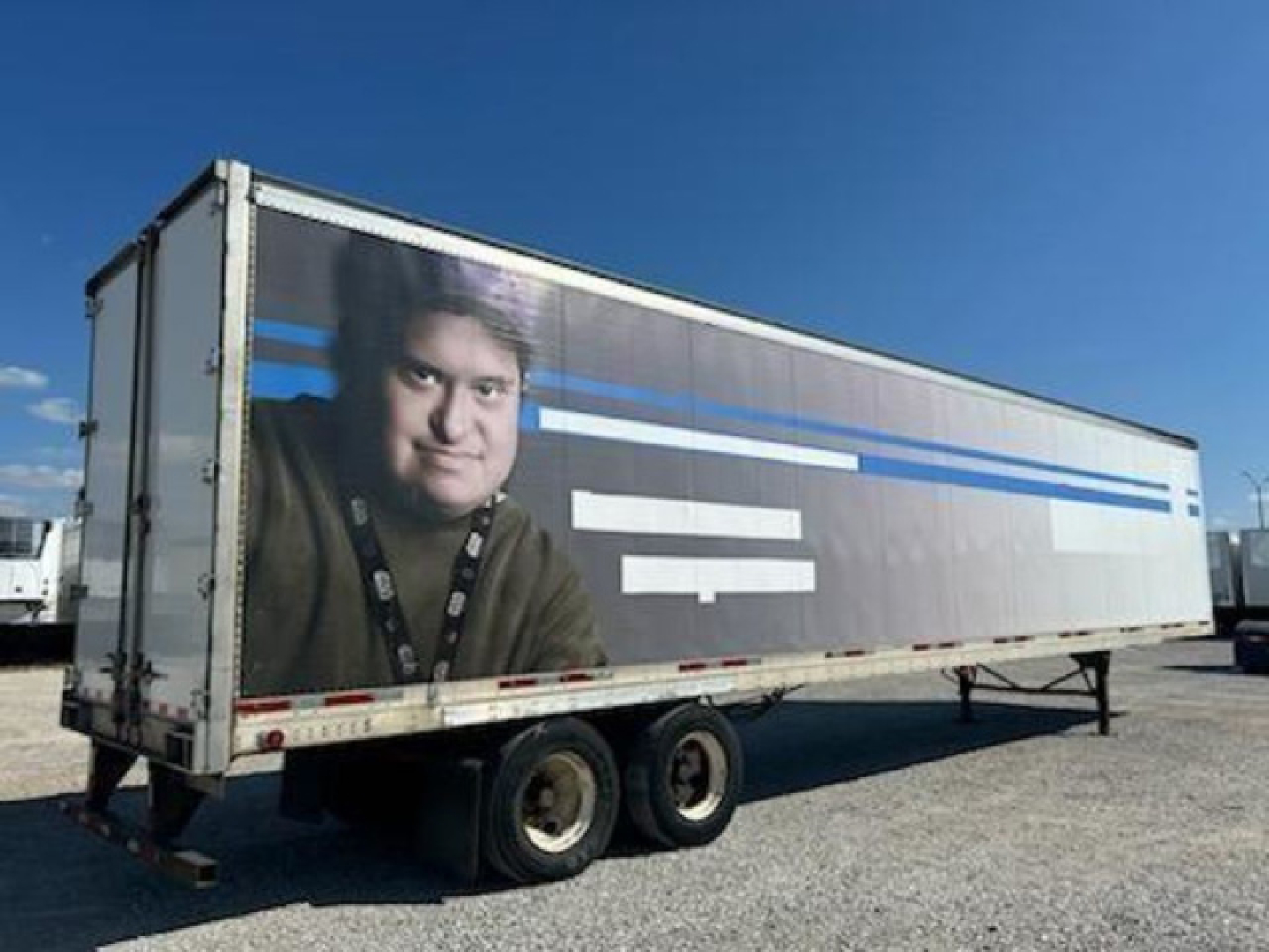 Trailer cargo van showing side graphics and dual rear axles under blue sky.