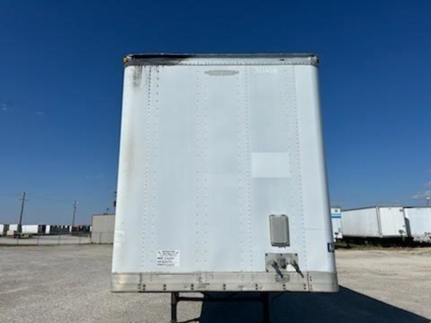 Trailer rear showing plain aluminum panel with riveted seams and a small access door near bottom right, no visible text.