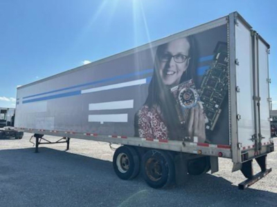 Trail-mobile van trailer showing exterior side graphic and dual rear axles with tires.