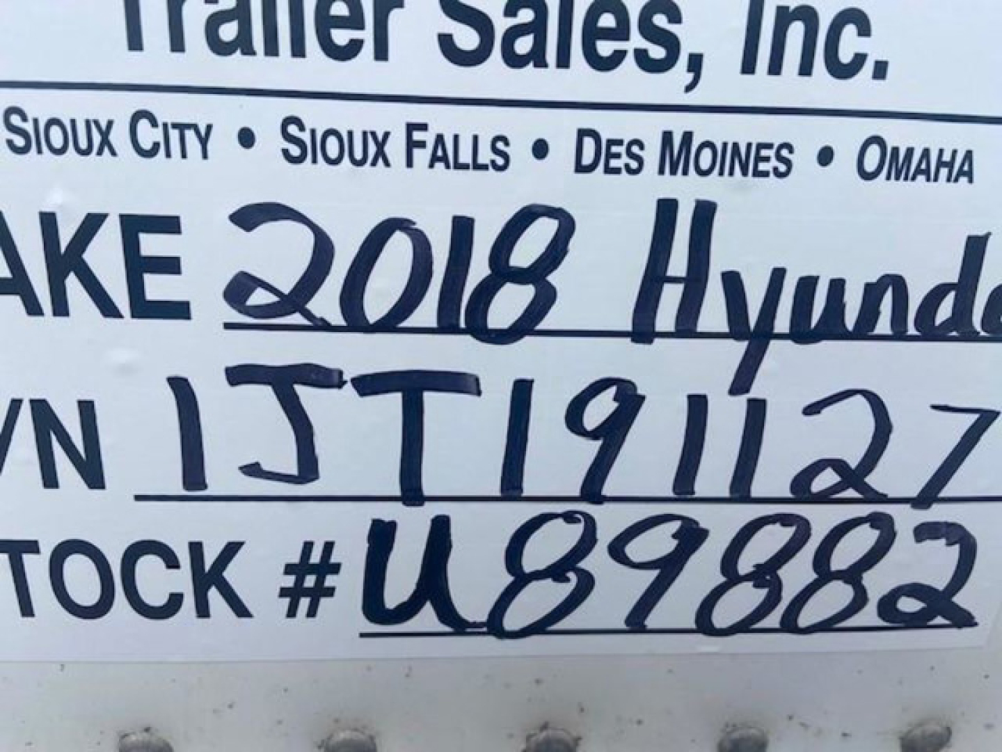 Sign with handwritten vehicle details: VIN partial '3H3V532C1JT191127', stock number 'U89882', '2018 Hyundai' written, and geographic dealership names (Sioux City, Sioux Falls, Des Moines, Omaha) in the background.
