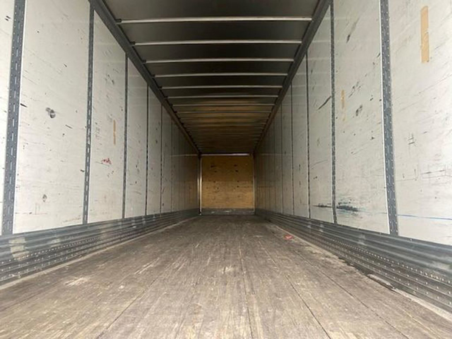 Trailer interior view showing cargo space with wooden floor and metal side walls, empty loading area.