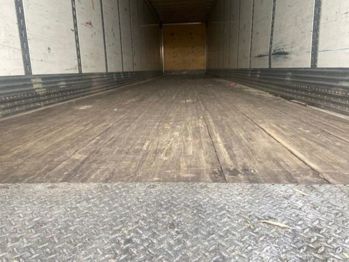 Trailer interior showing empty cargo area with wooden floor and metal side walls; open rear, Diamond tread metal at threshold.