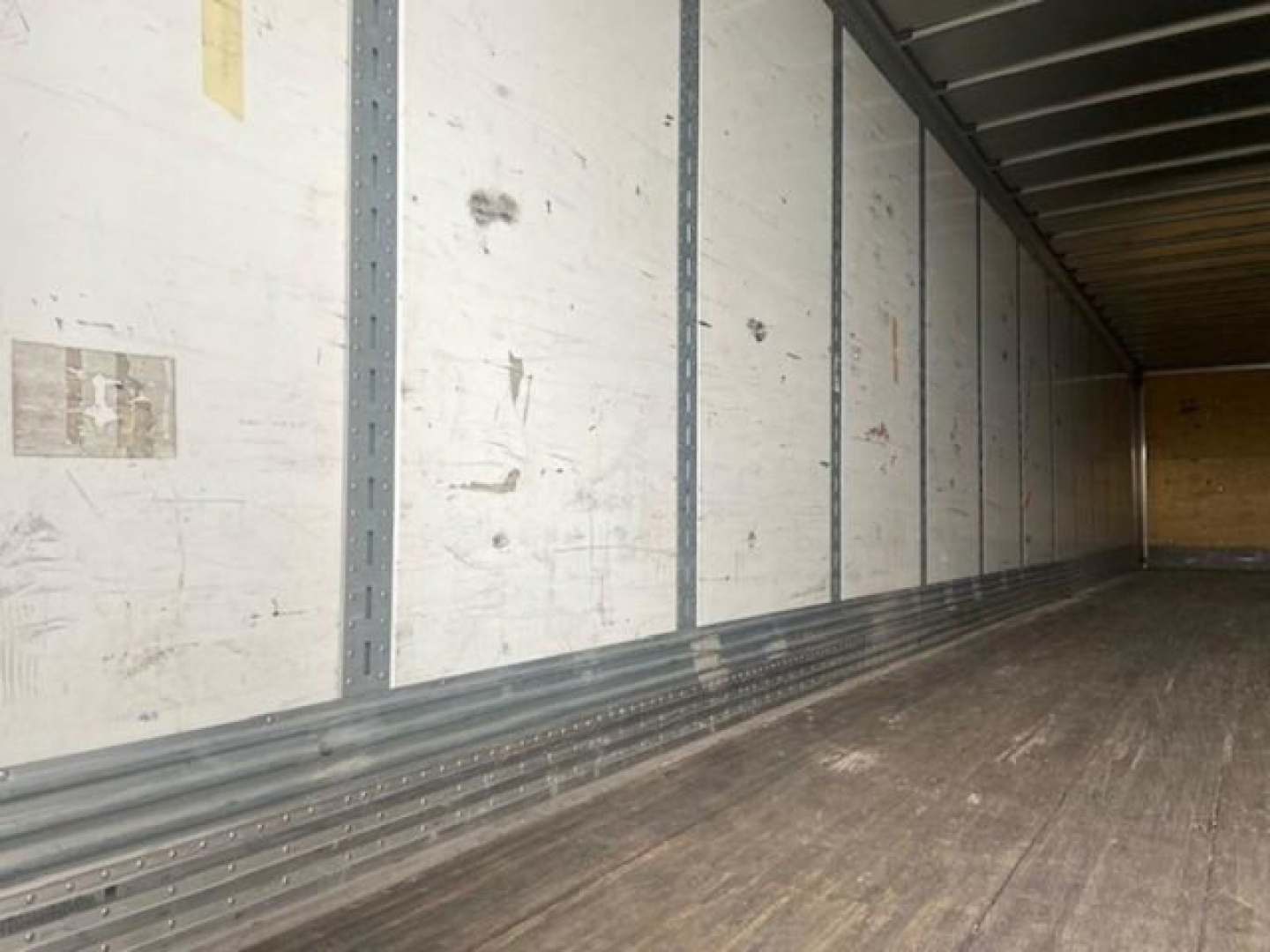Trailer interior showing empty cargo area with white side panels and metal rails, wooden floor, and cargo trailer walls.