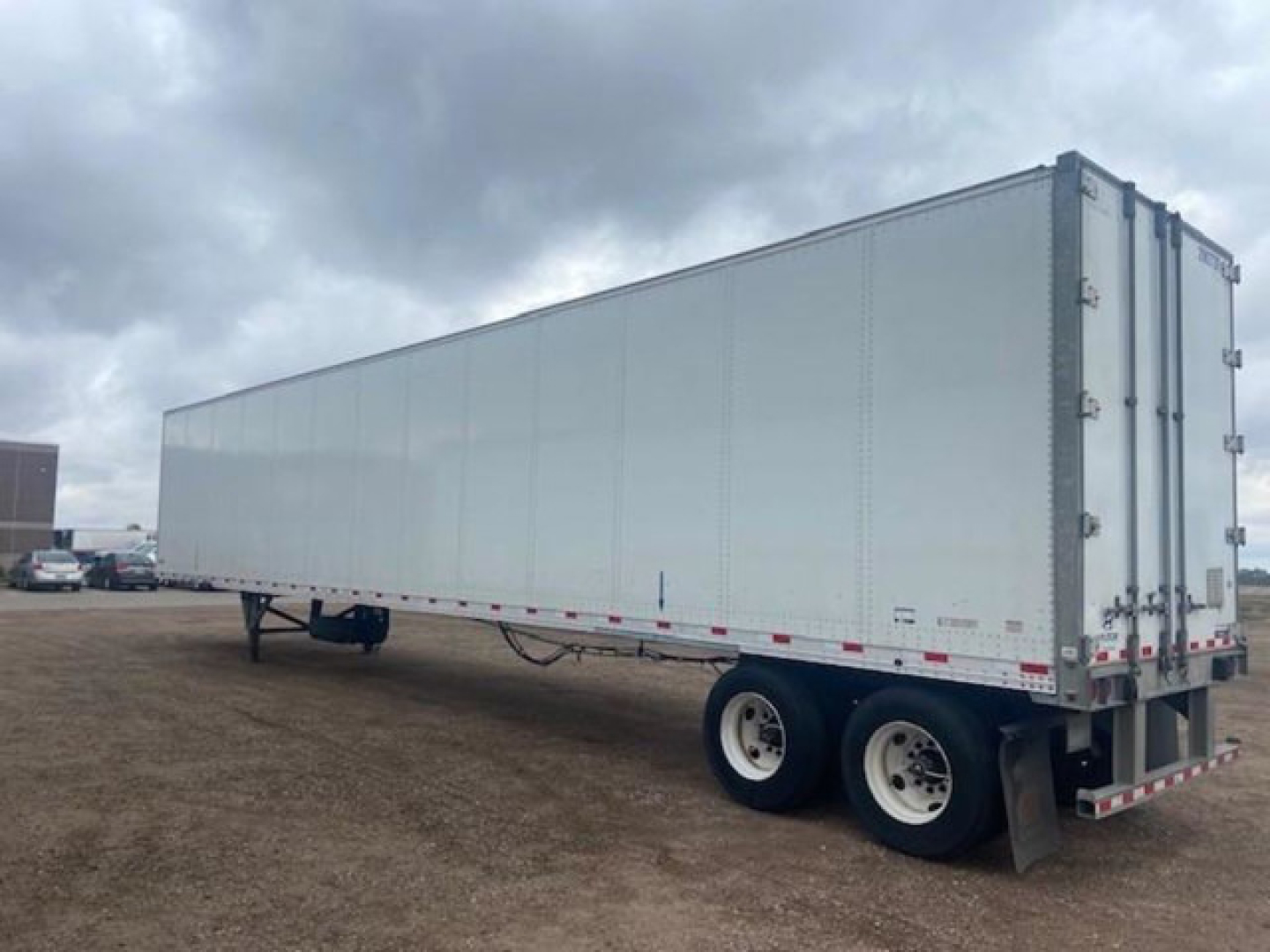 Trailer rear and side view of a white enclosed Hyundai van trailer on a dirt lot, dual rear wheels, rear doors closed, overcast sky