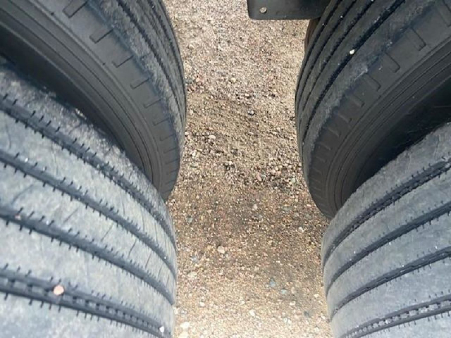 Tandem axle trailer tires and gravel ground viewed from between wheels.