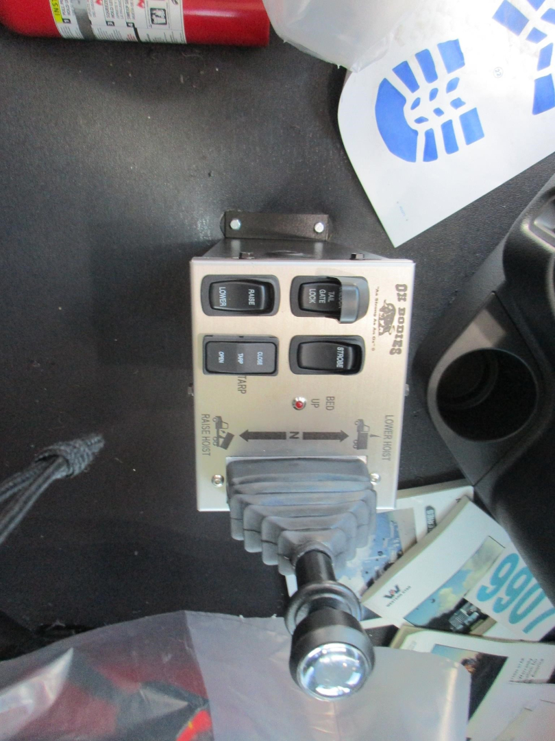 Control panel with four rocker switches and a joystick-like lever in a truck cab. Labels on the panel include ‘UP’, ‘DOWN’, ‘ON’ and ‘OFF’, with a rugged gray connector and a silver cylindrical knob. Visible items around inc