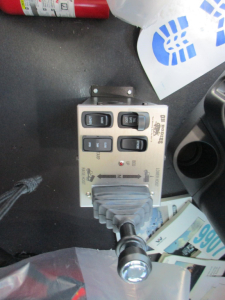 Control panel with four rocker switches and a joystick-like lever in a truck cab. Labels on the panel include ‘UP’, ‘DOWN’, ‘ON’ and ‘OFF’, with a rugged gray connector and a silver cylindrical knob. Visible items around inc