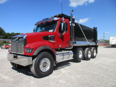 Red Western Star 49X dump truck with black dump body, chrome grille, and dual rear axles. Sunlit lot with blue sky.