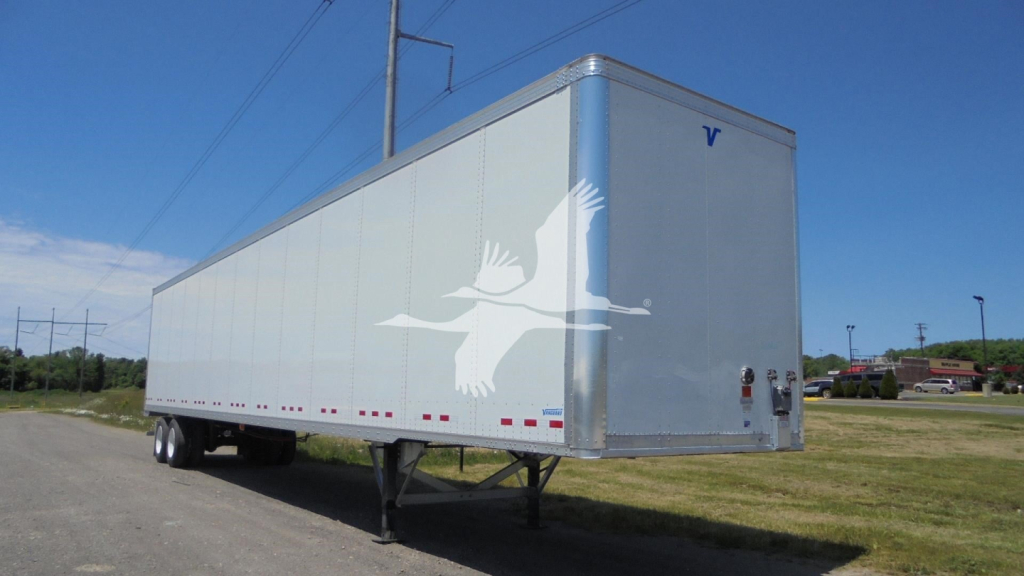 Trailer showing a Vanguard VXP with a large white bird logo on the side; dual rear doors; wheel chocks and landing gear visible; clear blue sky.