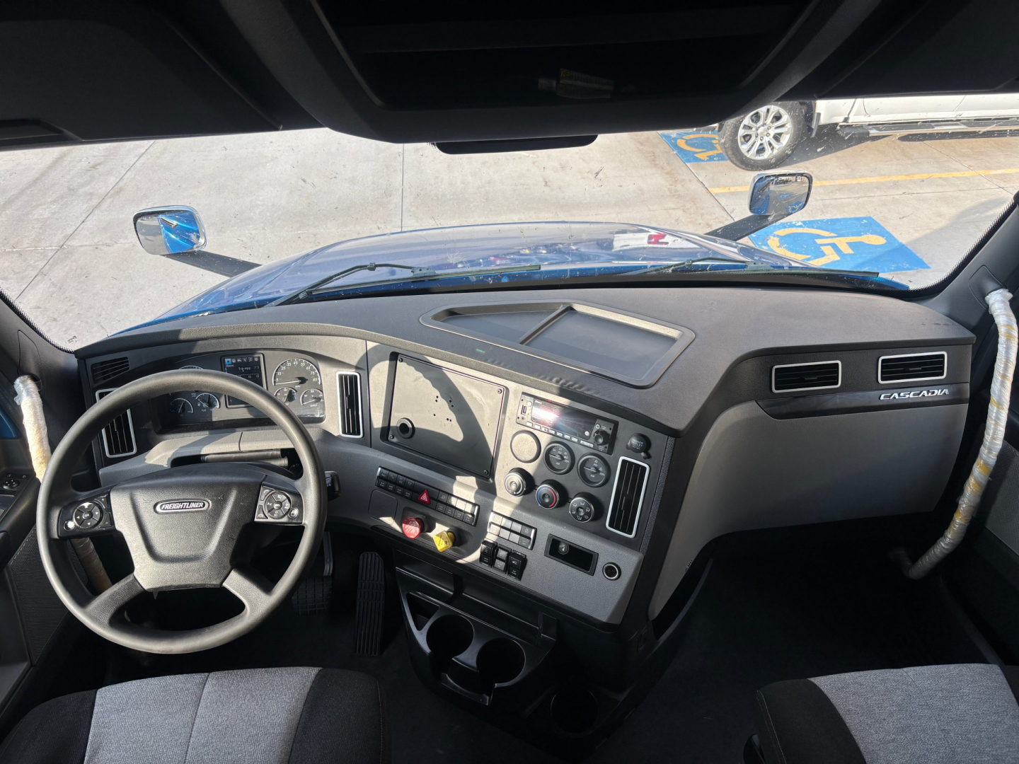 Cab interior of Freightliner truck showing steering wheel, dashboard controls, and center console.