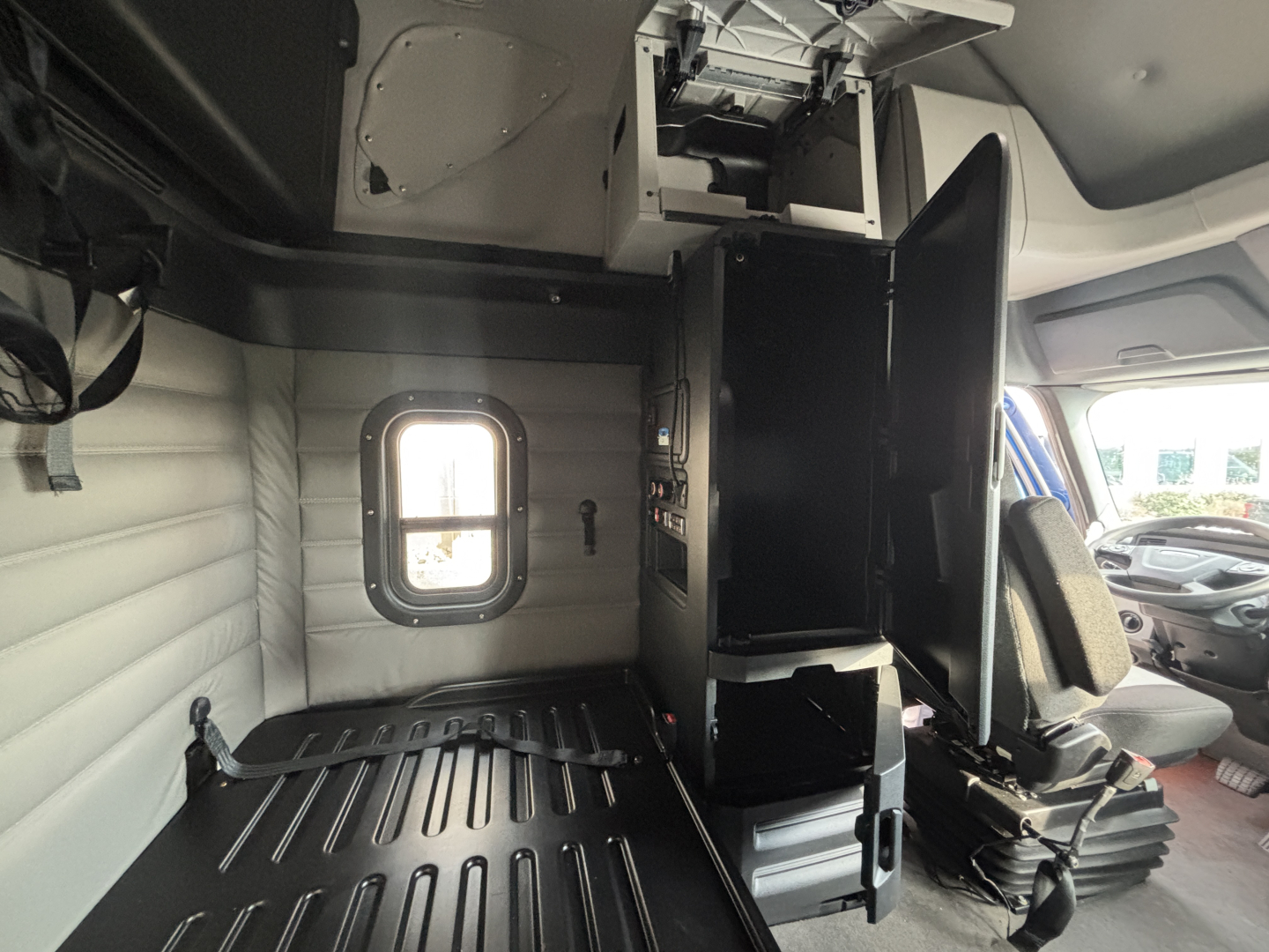Interior view of a Freightliner PT126064ST cab with a partition and storage compartments, side window, and driver seat visible.