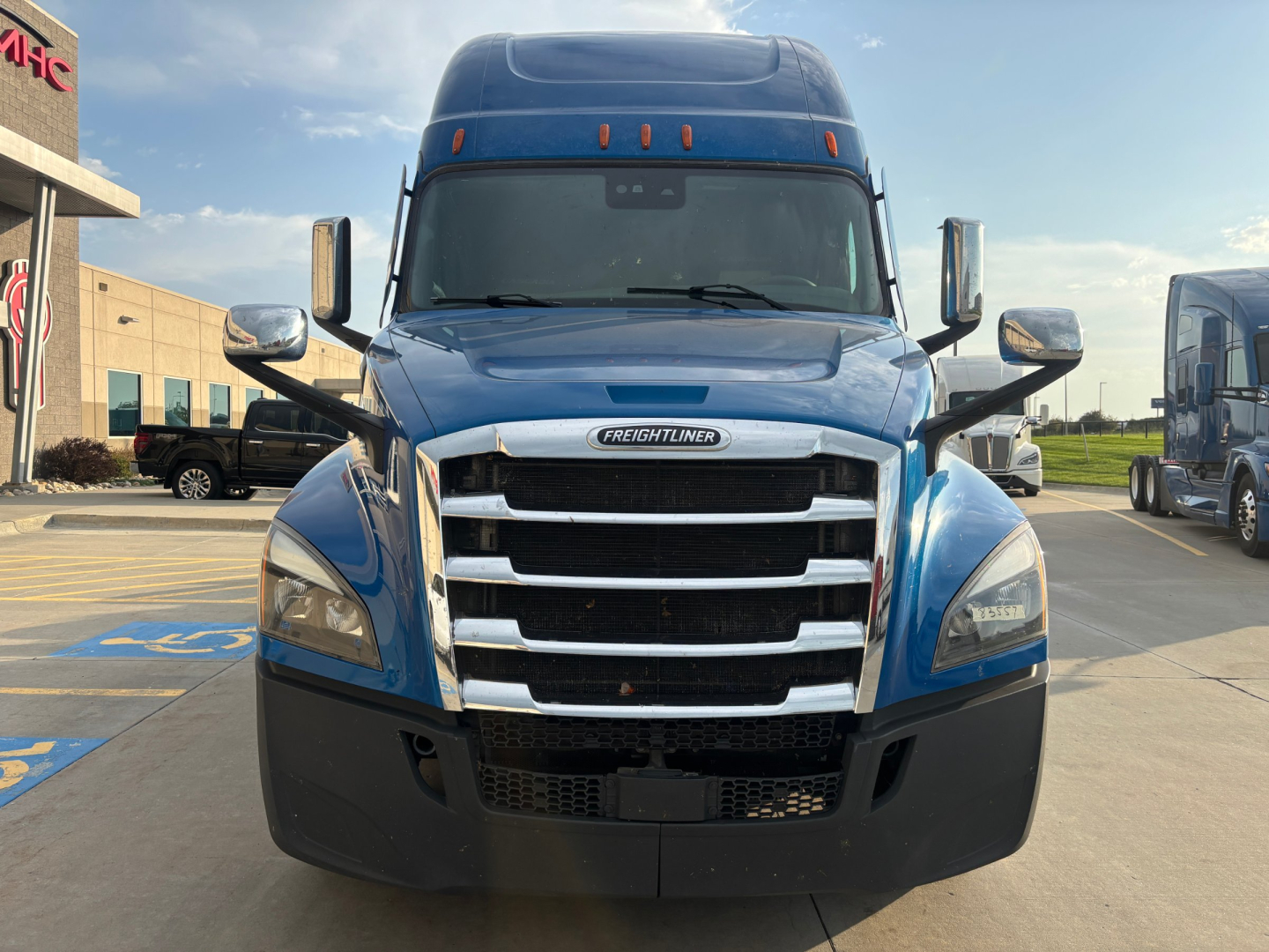 Front view of a blue Freightliner PT126064ST truck with large chrome grille, dual side mirrors, and high cab in a dealership lot.