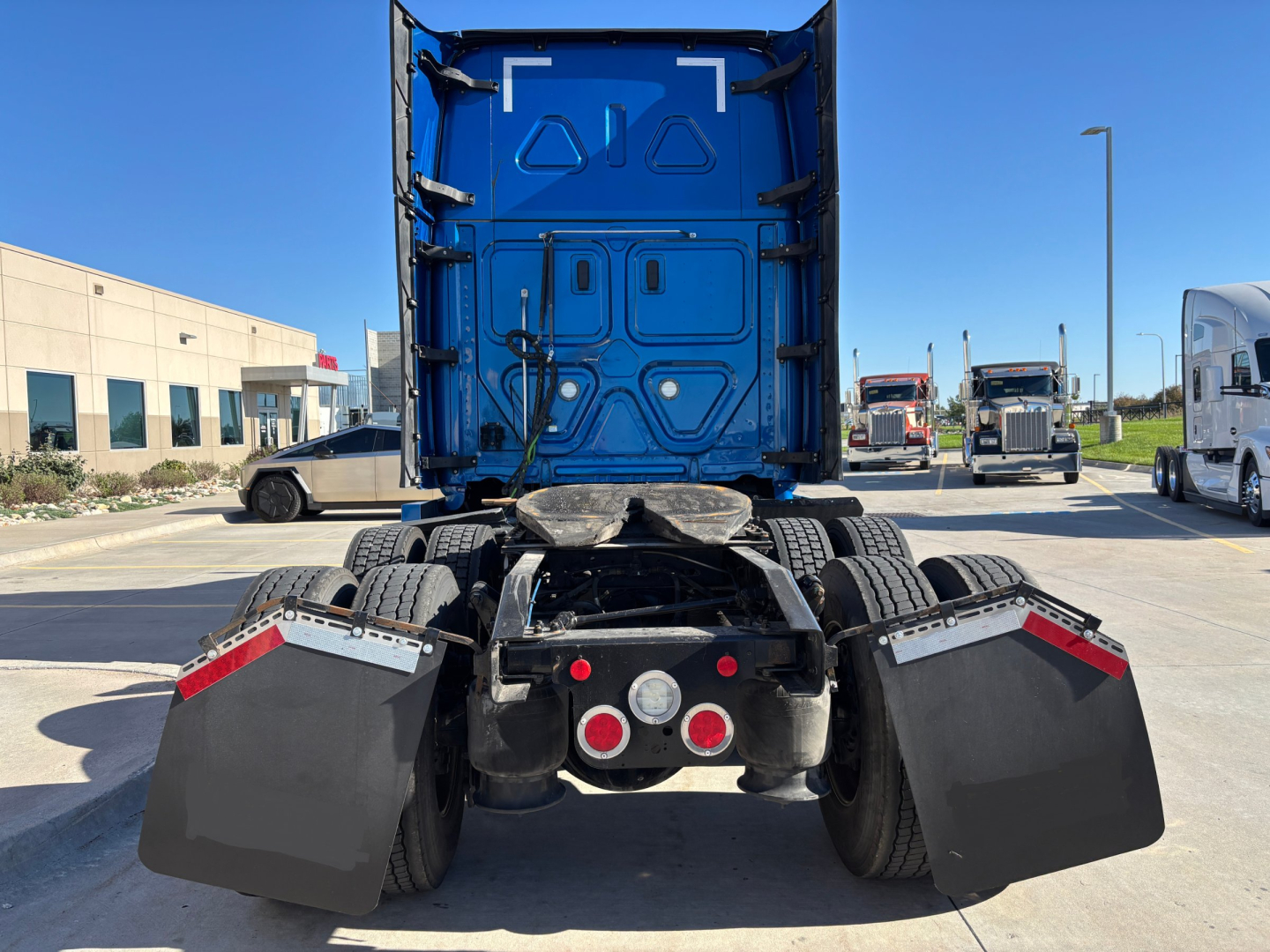 Rear view of a Freightliner PT126064ST sleeper tractor showing fifth wheel, mud flaps, and twin rear axles with blue cab behind.