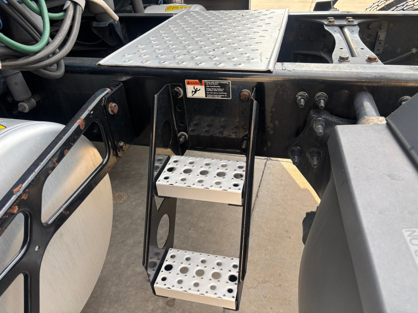 Freightliner PT126064ST truck chassis show metal diamond-plate steps and ladder under cab, with side tank, hoses, and mounting hardware visible.
