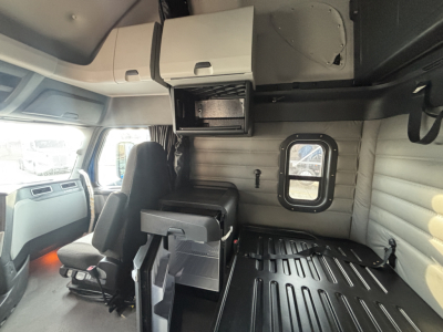 Truck cab interior view of a 2023 Freightliner PT126064ST showing sleeper area with storage cabinets and window.