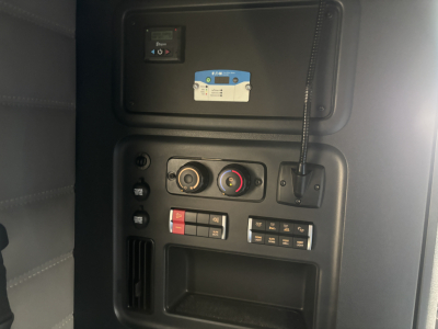 Cab interior panel of a Freightliner truck showing controls, switches, gauges and a blue card with text; visible labels include small circular knobs and a keypad area.
