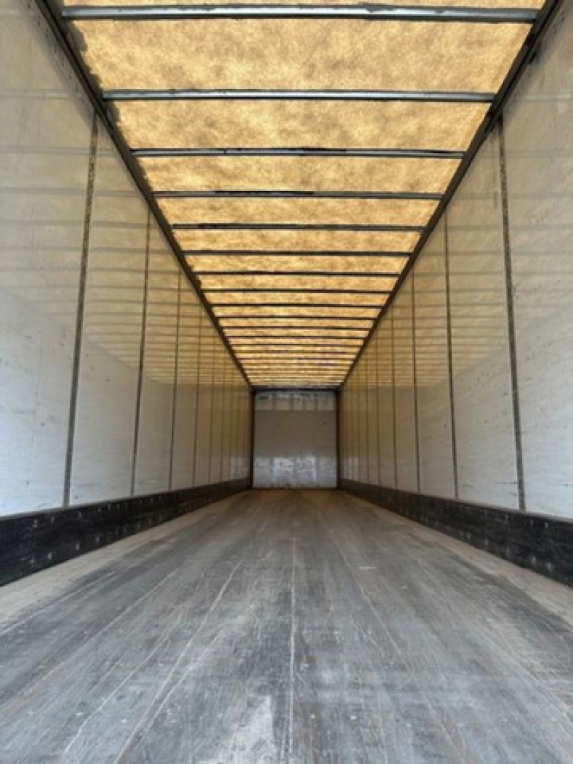Trailer interior image showing long enclosed cargo space with light panels on roof and side walls; empty floor with textured rubber/wood; rear door opening visible.