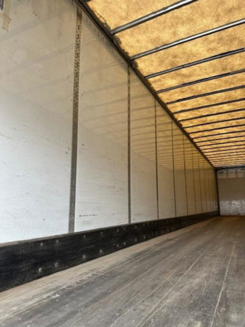 Trailer interior showing long aluminum side walls with vertical linings and a wooden floor in a cargo van.