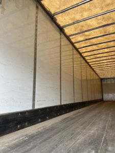 Trailer interior showing long aluminum side walls with vertical linings and a wooden floor in a cargo van.