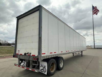 Trailer side and rear showing a white Wabash van trailer with dual rear axles and a raised rear loading area.