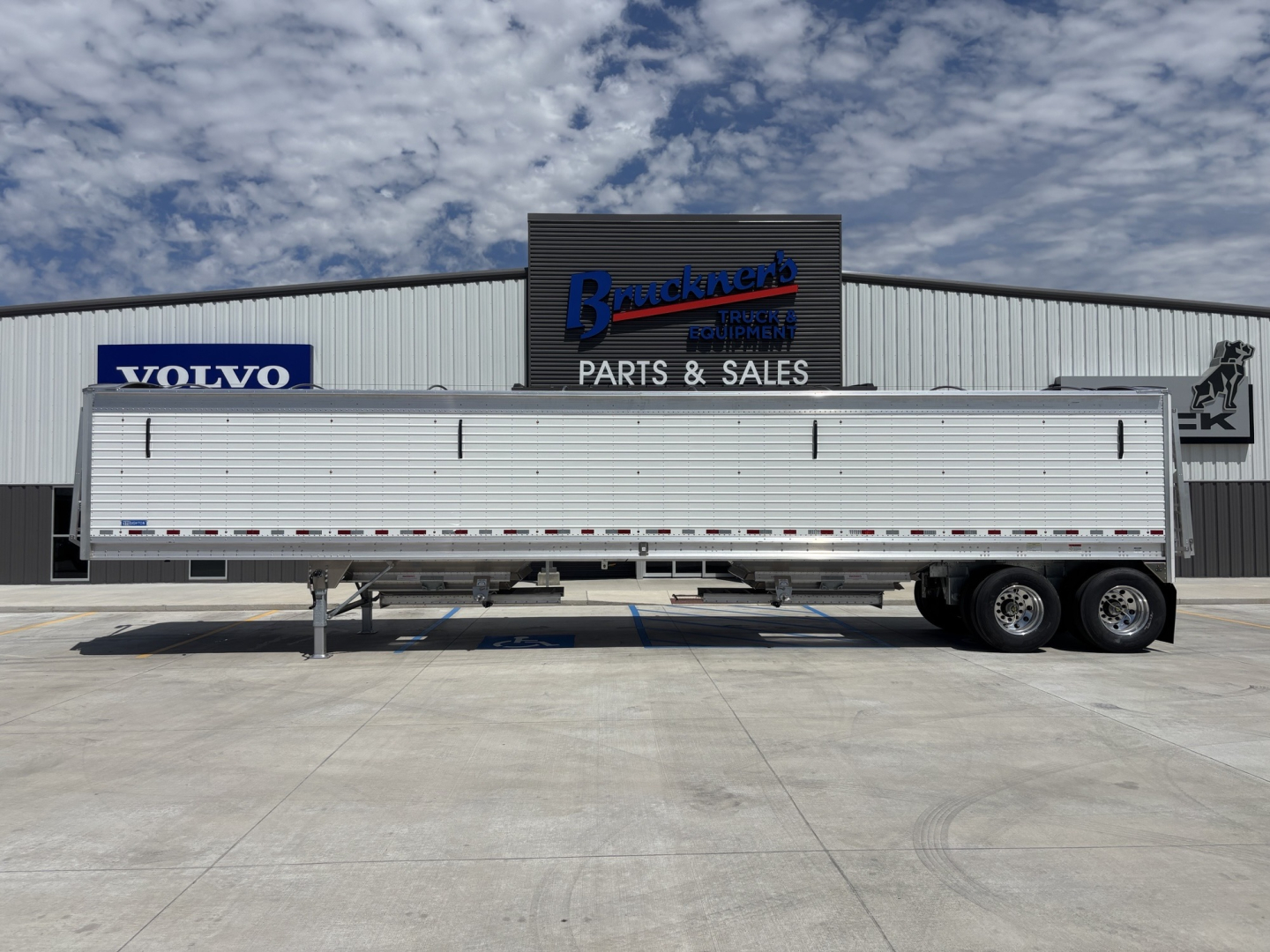 Trailer side view of a 2026 Stoughton 43' alum grain hopper with 80" sides, parked in front of a parts and sales building.