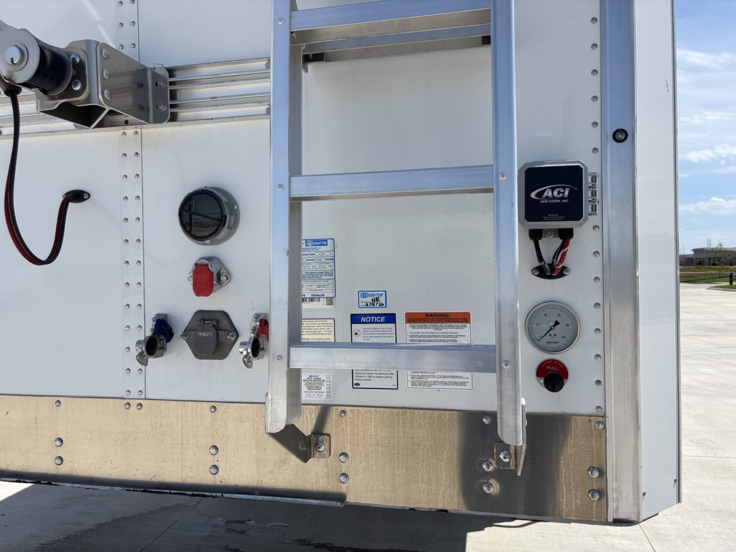 Stoughton 43' aluminum grain hopper trailer rear panel showing control valves, gauge, and ladder with label stickers.