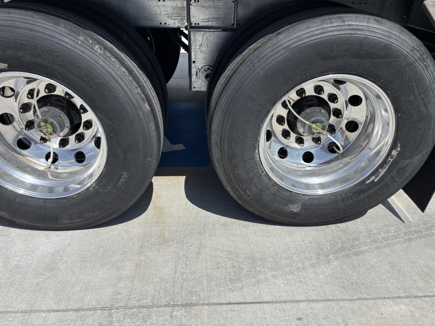 Dual rear trailer wheels with polished rims and tire treads visible under a hopper trailer.