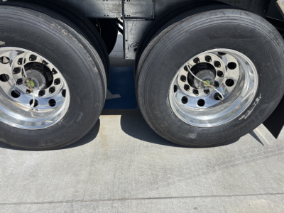 Dual rear trailer wheels with polished rims and tire treads visible under a hopper trailer.