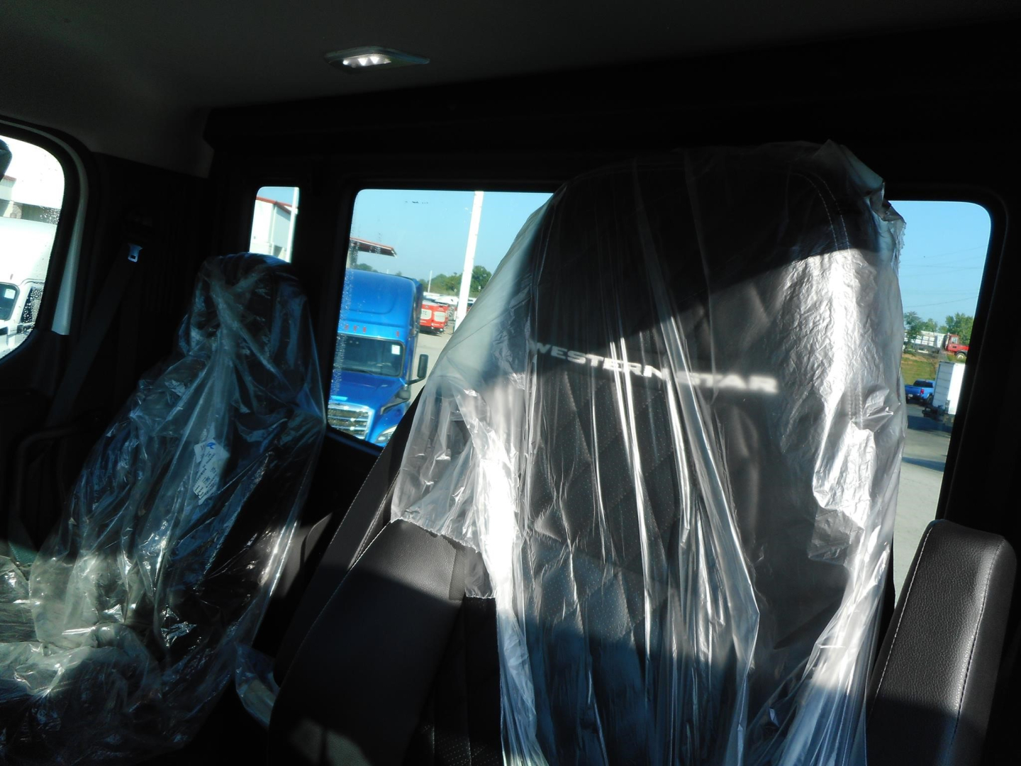 New Western Star 49X day cab interior view with plastic-covered seats and dashboard; visible window showing parking lot.
