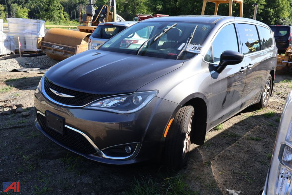 2020 Chrysler Pacifica minivan in a salvage yard, front-left view, gray exterior with chrome grille and alloy wheels.