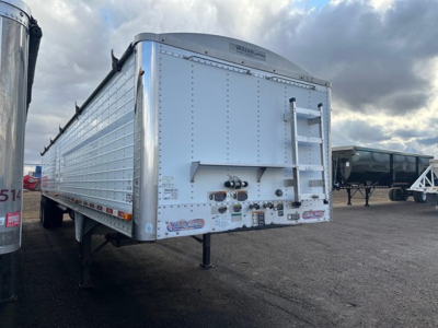 Trailer bay showing a white Wilson hopper trailer with rear doors and a ladder, side decals, and a landing gear against a cloudy sky.