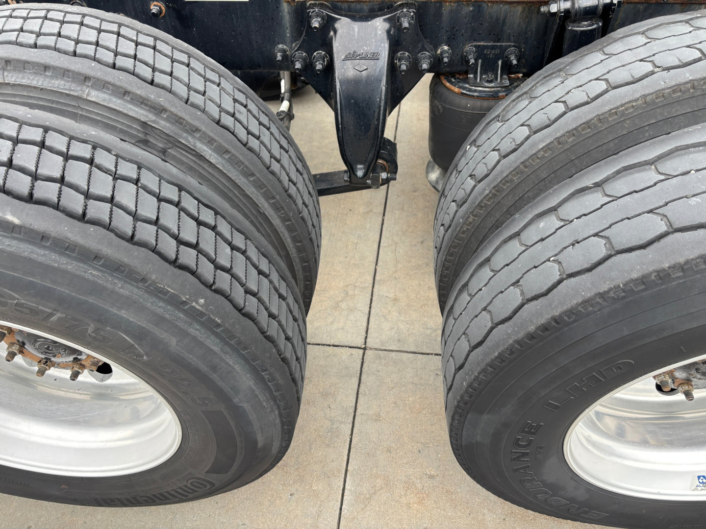 A Freightliner truck chassis view with dual rear wheels and tires, showing suspension and frame components.