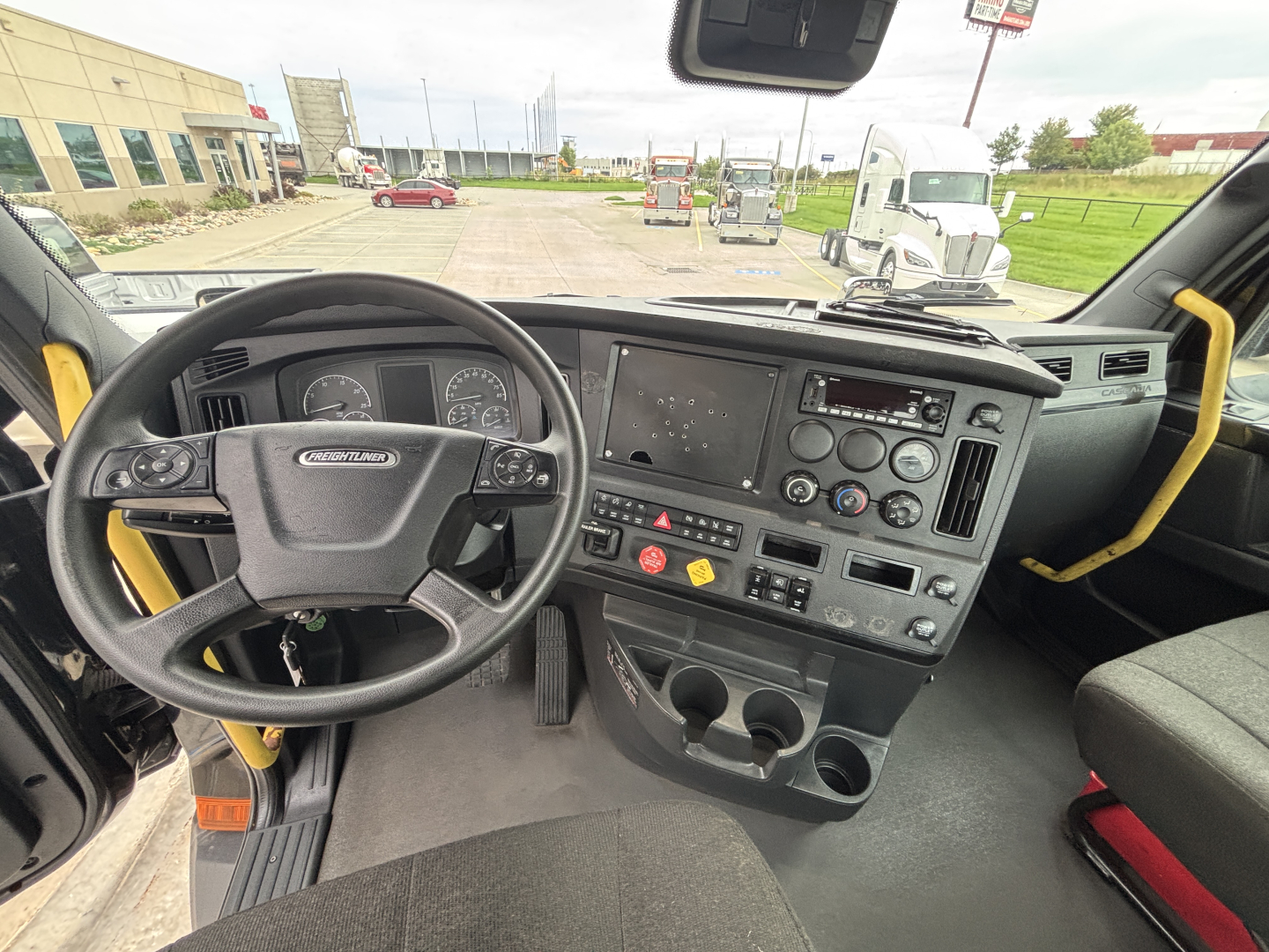 Cab interior of a Freightliner truck showing steering wheel, dashboard with gauges, center console, and cup holders.