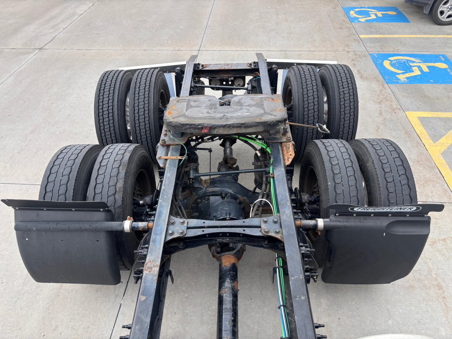 Rear view of a Freightliner truck chassis showing dual rear axles, fifth wheel area, and exposed drivetrain with some rust on frame.