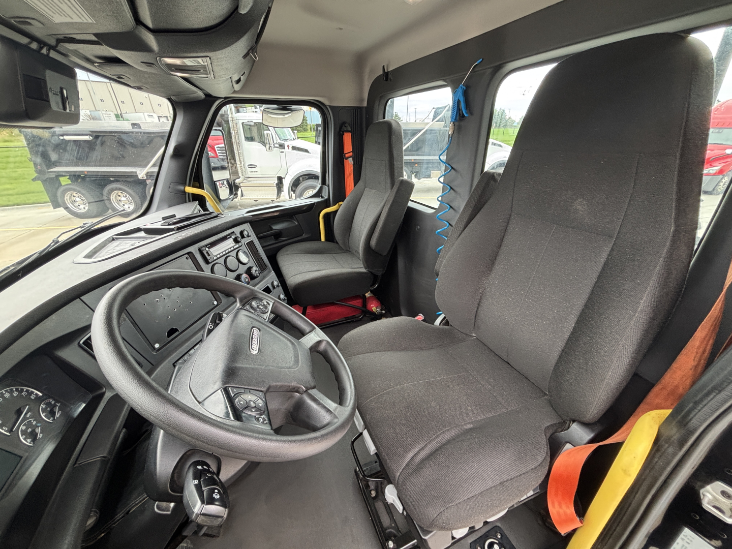 Cab interior of Freightliner truck showing steering wheel and driver's seat with dashboard controls.