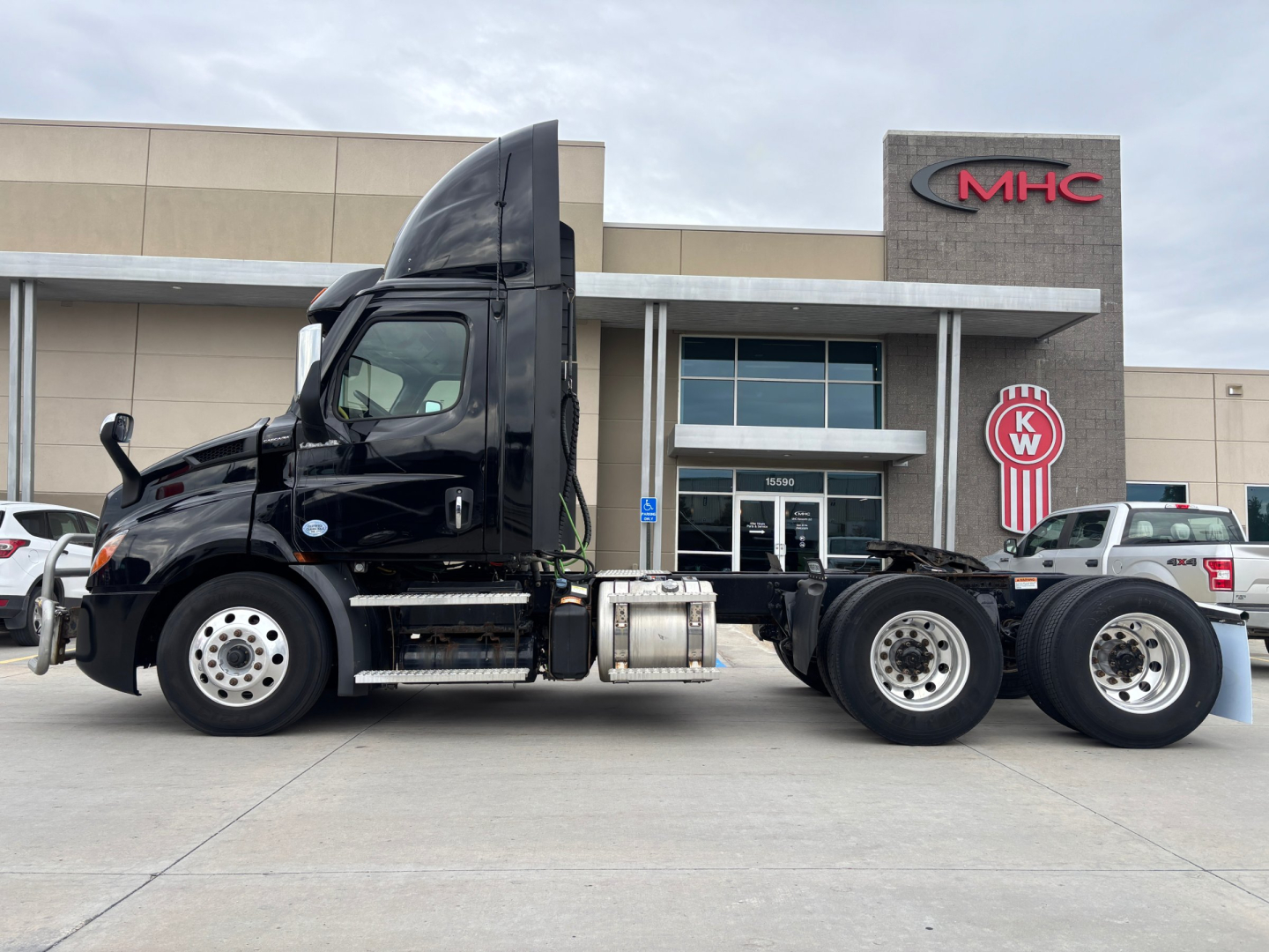 Truck chassis side view showing Freightliner PE11664DC with absence of trailer and VIN 3AKJHTDVXPSNK5917 visible on listing; dealership building in background.