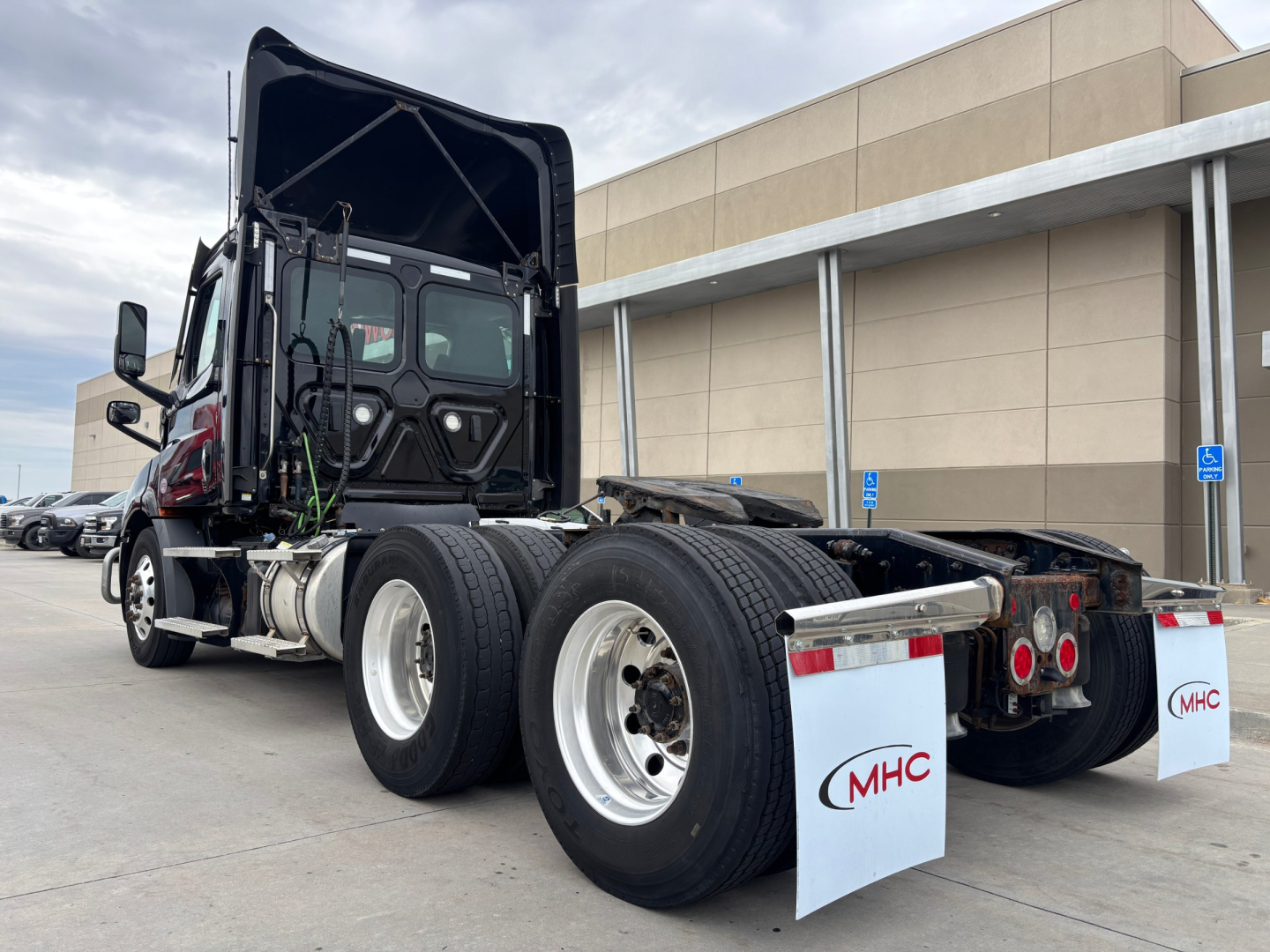 Truck rear view showing multiple wheel axles and cargo area with folded sleeper cab; Freightliner PE11664DC tag and wheel components visible.